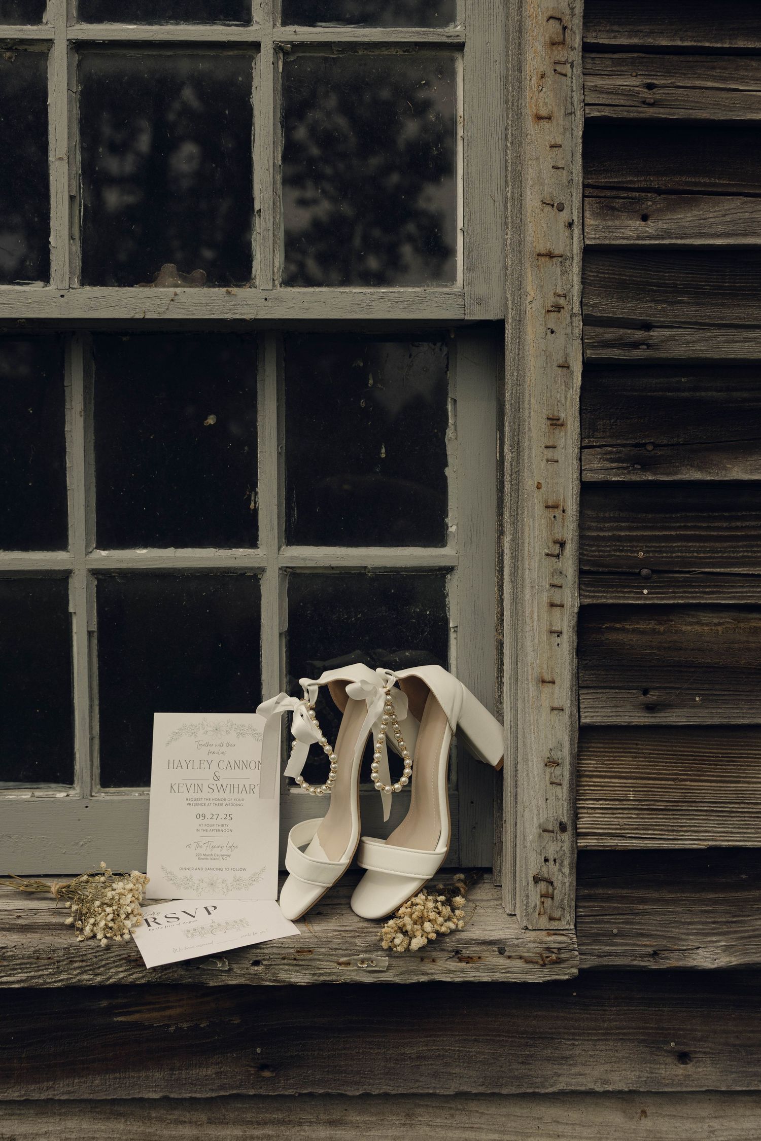 White wedding shoes and invitation cards rest on a weathered wooden windowsill in a vintage setting.