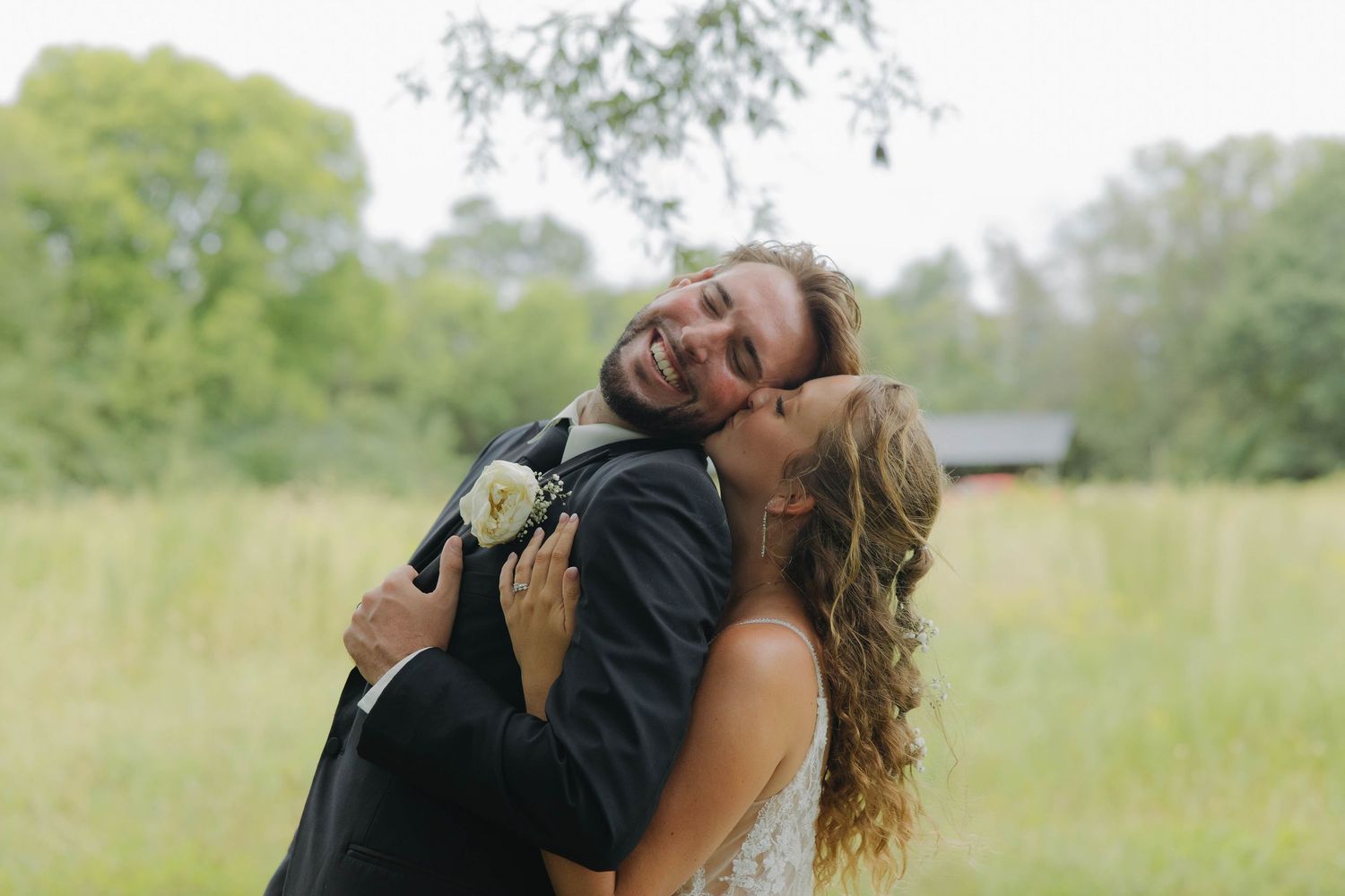 A couple in formal attire dances and embraces in a grassy outdoor setting.