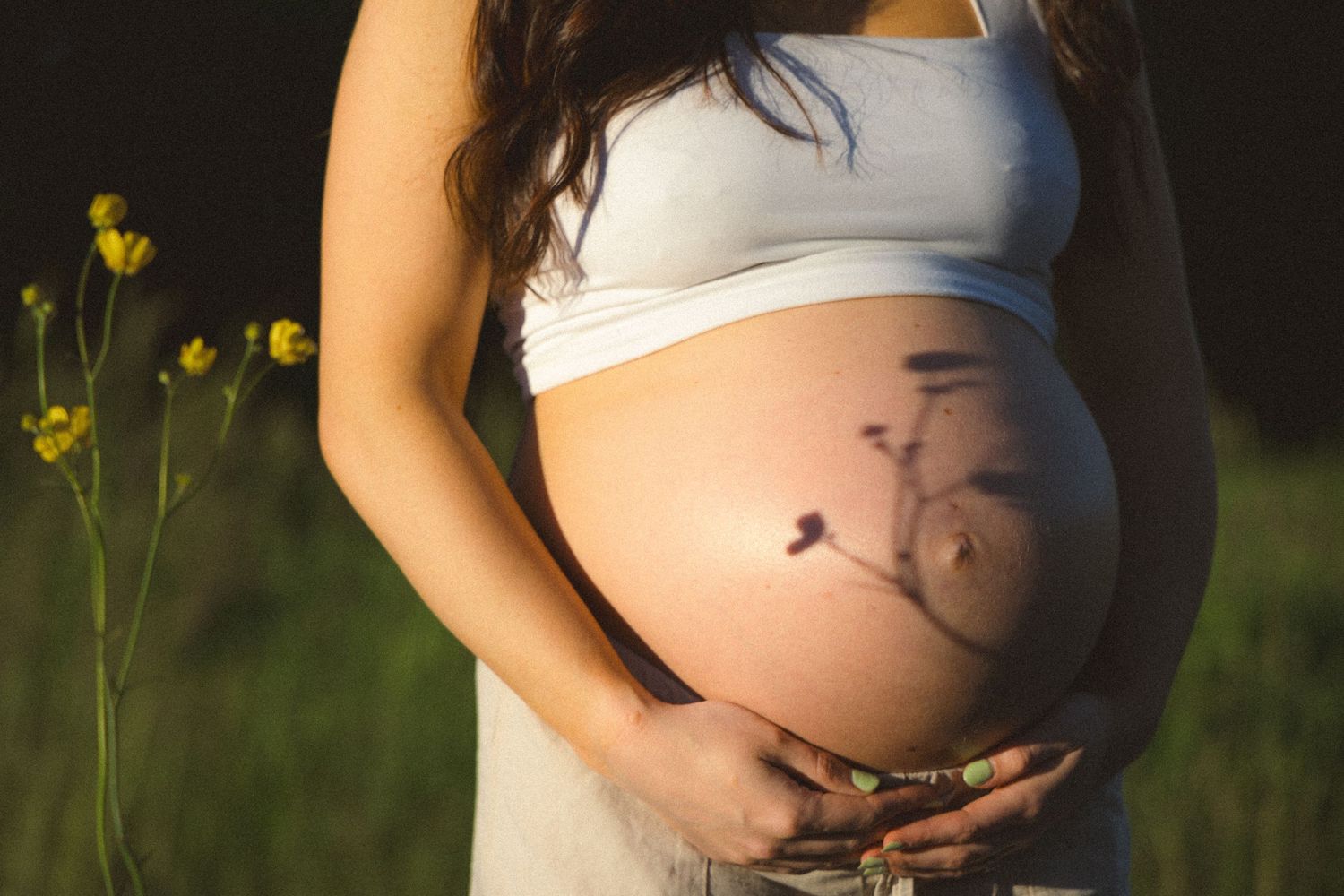 Golden hour capture of a pregnant belly with the shadow of a flower on it during a maternity photoshoot in Vancouver, BC.