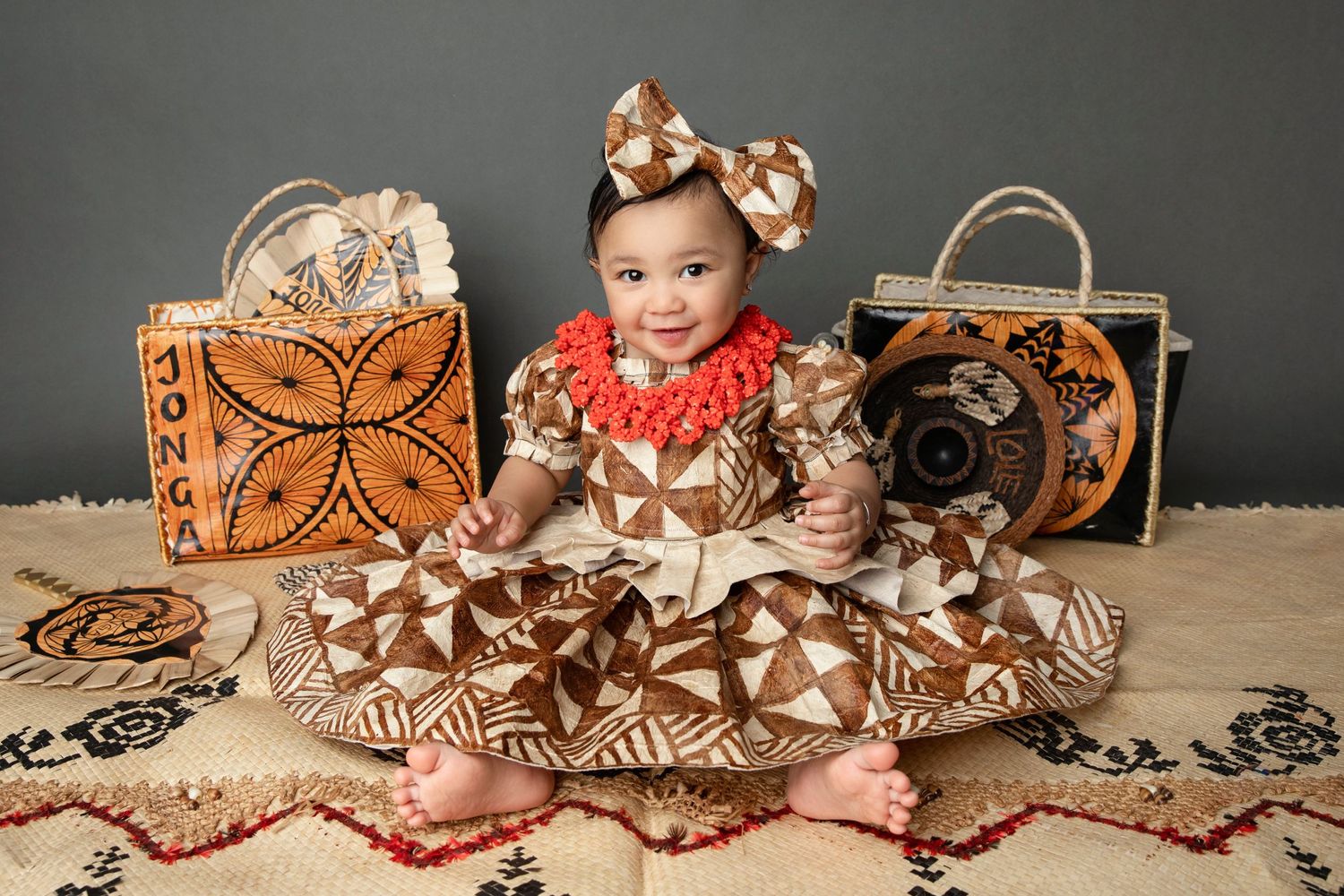 Happy baby in traditional dress sitting on patterned rug with decorative bags.