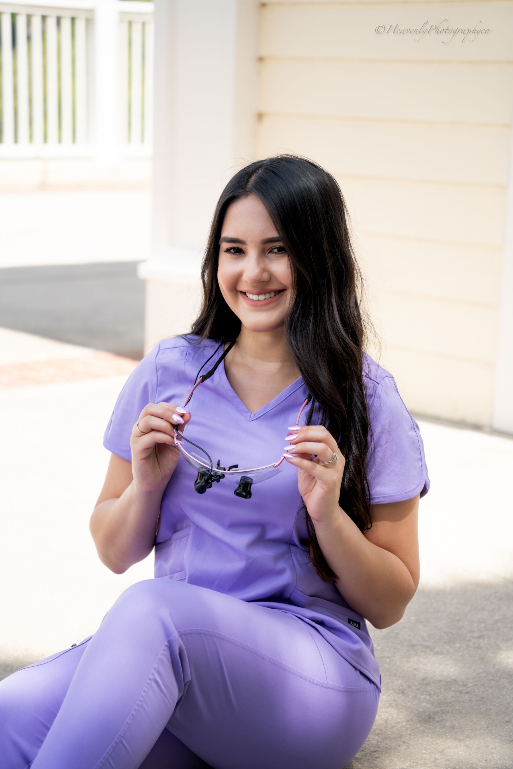 Healthcare worker in purple scrubs poses with nursing pins outdoors.