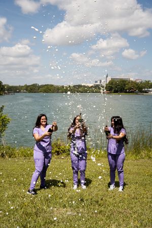 Healthcare graduates throw confetti by a lake in celebration.