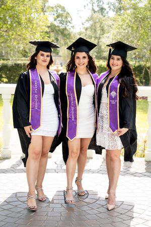 Graduates in caps and gowns show off their purple sashes while sitting together.