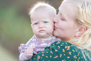 Mom lovingly kisses her baby during a family photo session, capturing a sweet moment as the baby looks curiously at the camera.