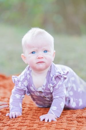 Sweet baby with bright blue eyes, crawling and looking curiously at the camera, capturing a truly adorable and captivating moment.