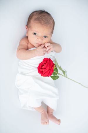 Newborn baby wrapped in a soft white swaddle with a cute red flower on top, capturing a serene and sweet moment.