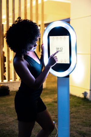Lady captured interacting with the photo booth screen, intrigued by the fun and engaging experience at the event.