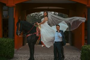 A bride's veil flows dramatically in the wind as she poses with others under an archway.