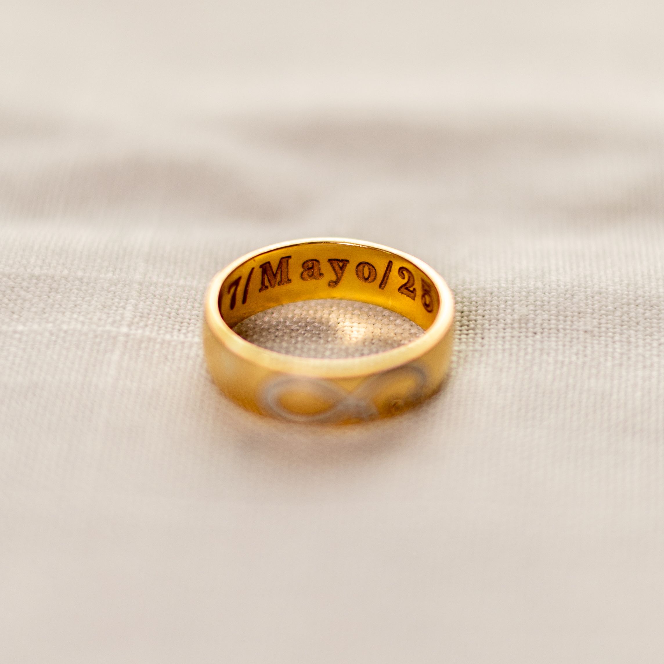 Close-up of a gold wedding band with engraved text on white fabric.
