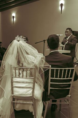 A wedding ceremony in progress with a couple seated in Chiavari chairs listening to the officiant.
