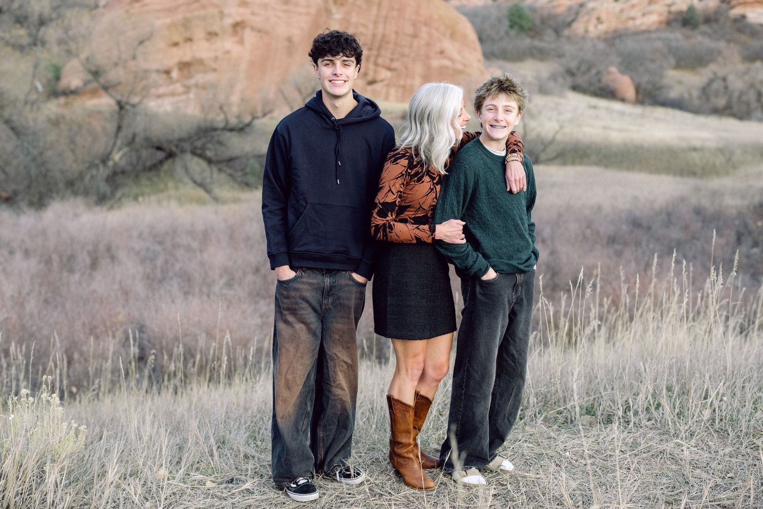 Three people smile together outdoors with trees in the background.