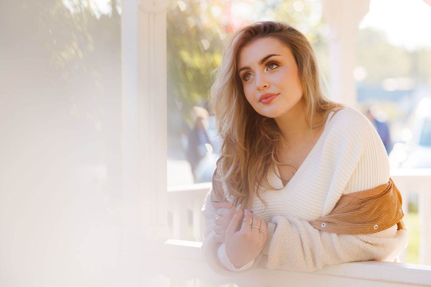 Natural light portrait of person in white sweater sitting thoughtfully by window with soft dreamy background.