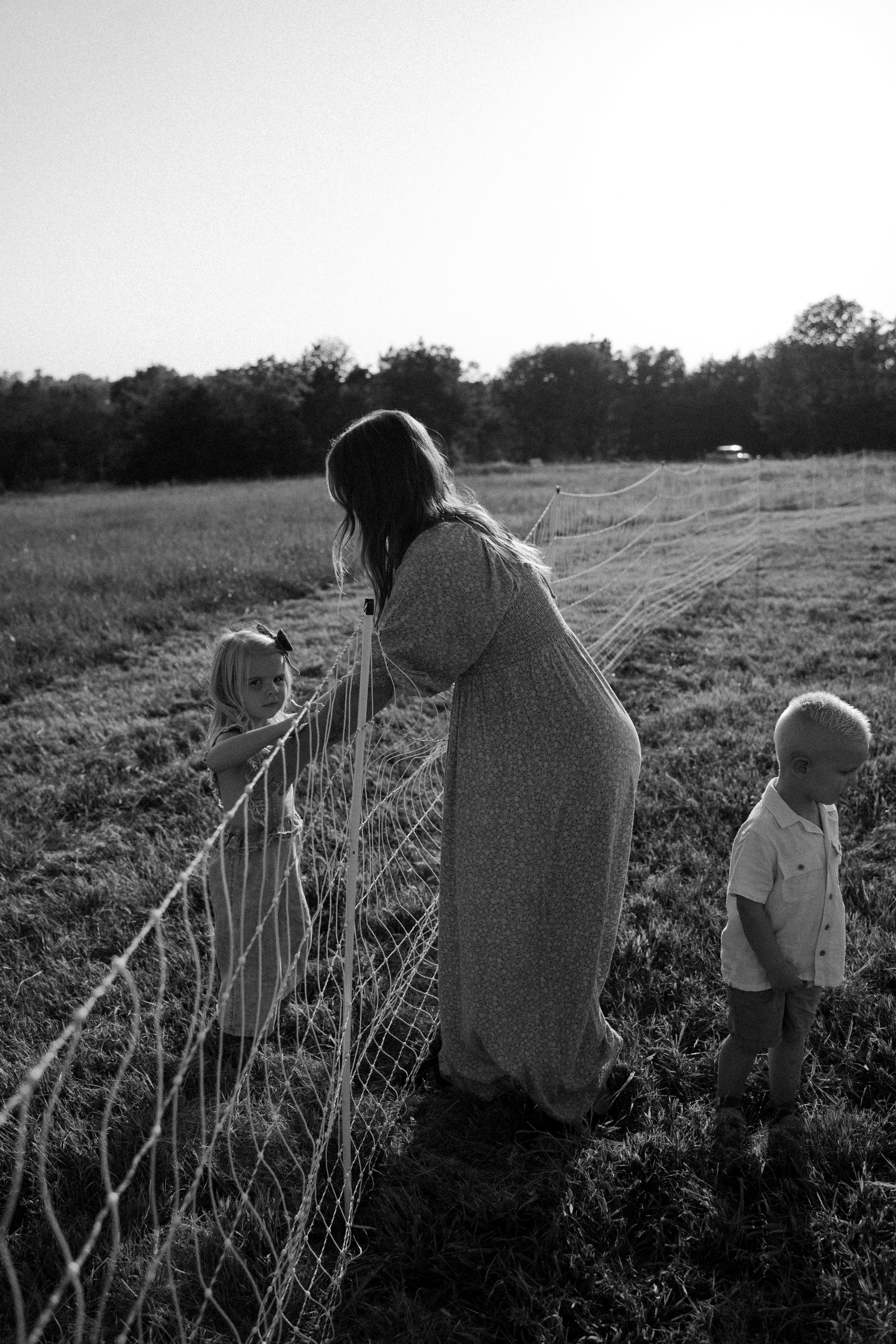 Black and white photo of people sitting by a wire fence at sunset.