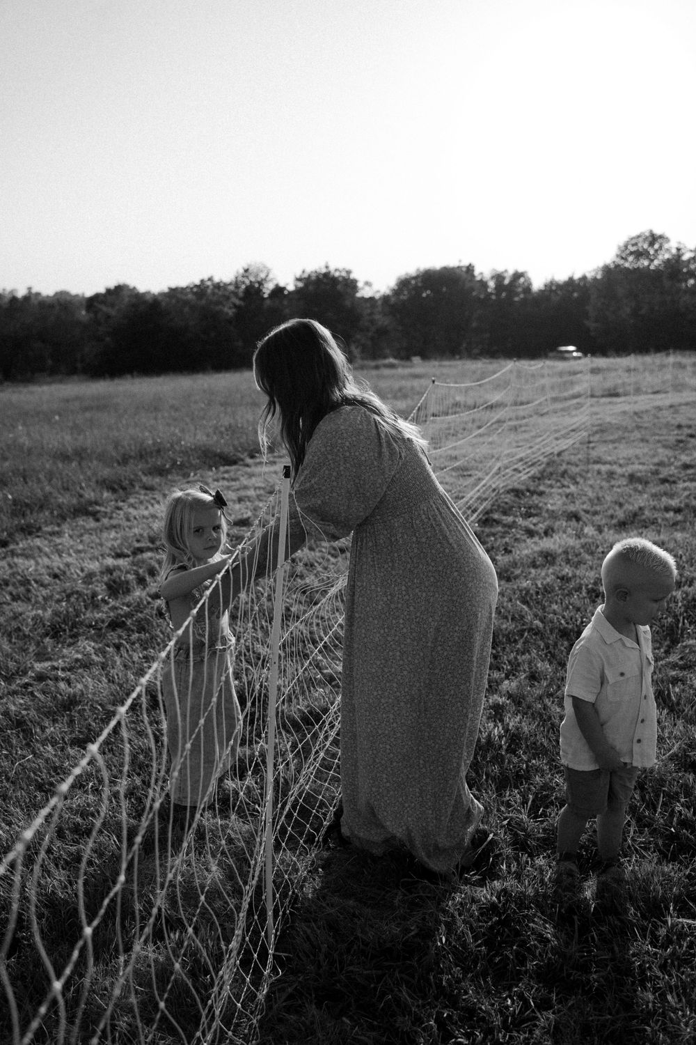 Black and white photo of people sitting by a wire fence at sunset.