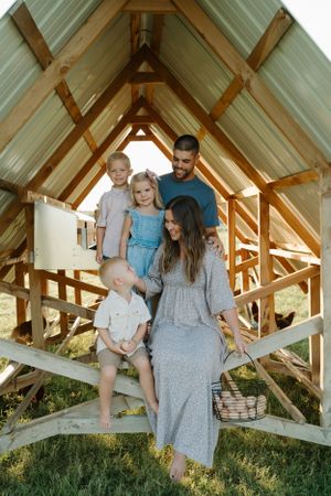 Family gathered under wooden shelter during outdoor photoshoot at sunset.