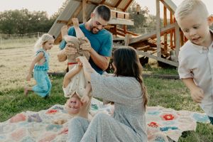 Candid family moments captured on a blanket during sunset with wooden shelter in background.