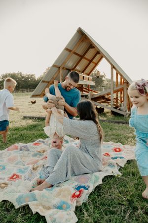 Family having fun and playing together on a patterned blanket outdoors.