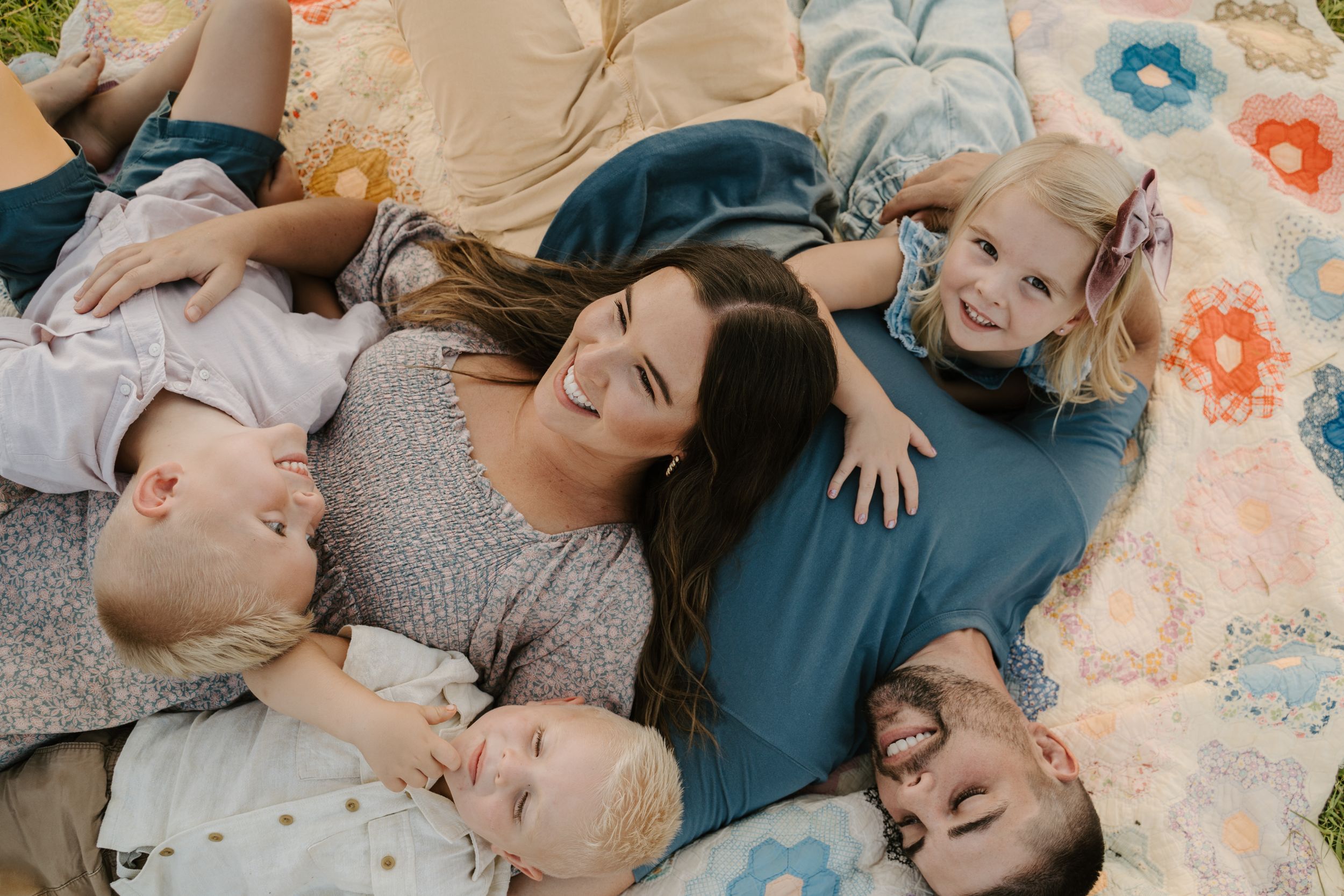 Family enjoying playful moments together on a colorful blanket during an outdoor photoshoot.