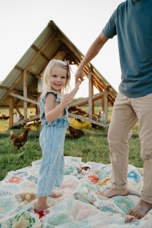 Children playing on a colorful quilt spread on grass near a wooden shelter.
