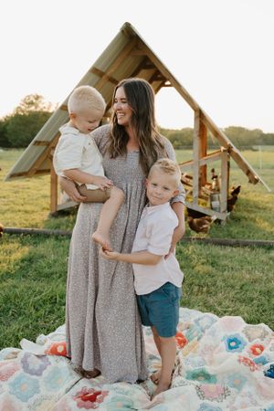 A tender family moment captured on a floral blanket with a rustic shelter in the background.