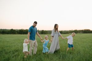 Family walking together through a green field at sunset with wooden structure in background.
