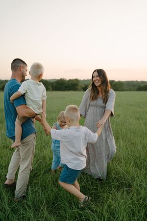 Family walking through tall grass field during golden hour photoshoot.