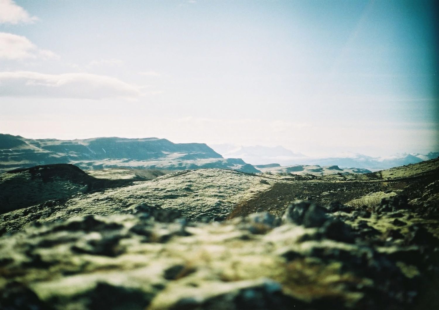 Scenic mountain landscape with rolling green hills and misty peaks stretching into the distance under cloudy skies.