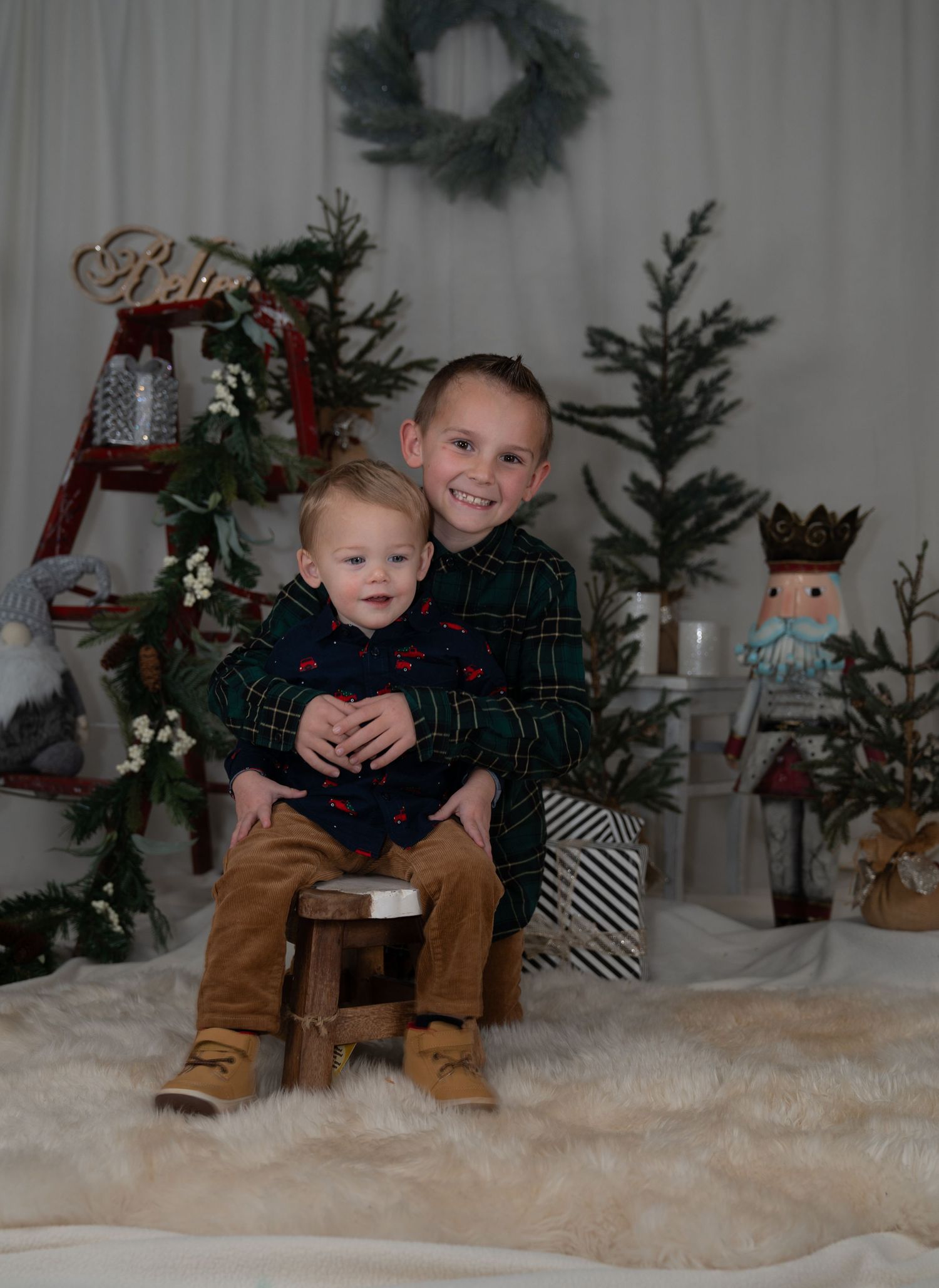 Two children pose together on a white fluffy rug with Christmas decorations in the background.