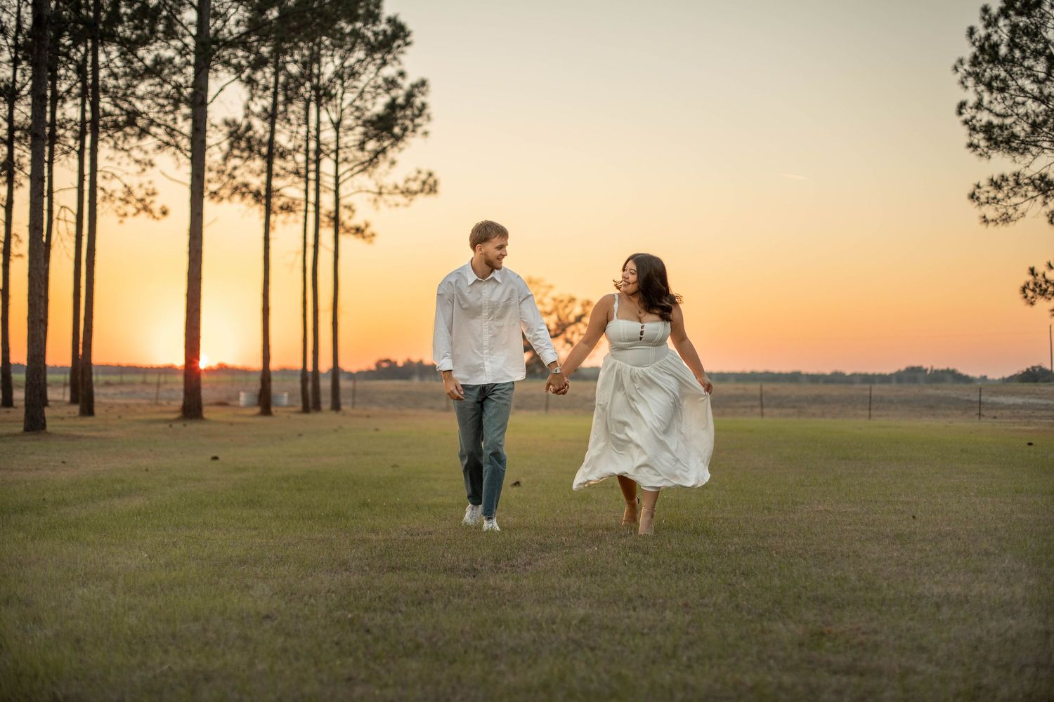 A couple running in a field at sunset at their wedding venue for an engagement session.