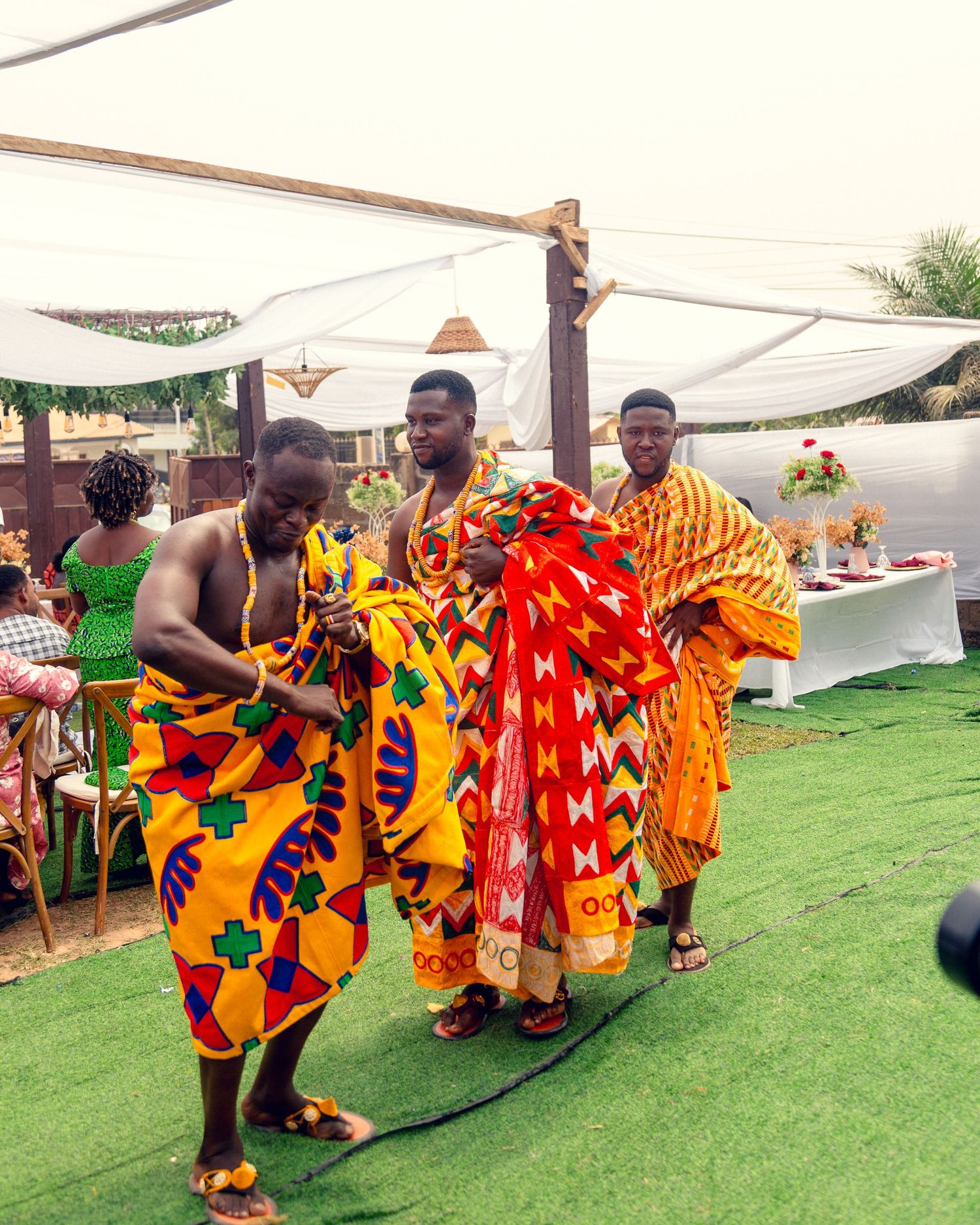 Traditional African celebration with people wearing vibrant kente cloth and traditional attire dancing at an outdoor event.