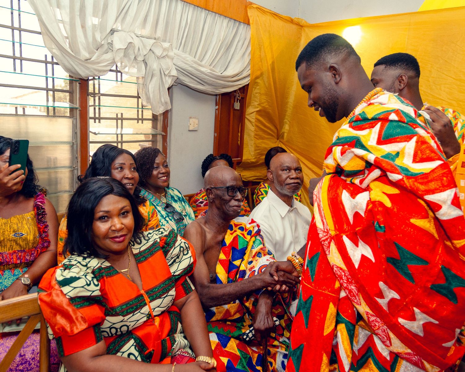 Traditional African celebration with people wearing vibrant kente cloth and traditional attire dancing at an outdoor event.