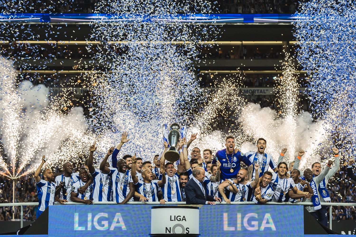Soccer team celebrates championship victory on stage with confetti and pyrotechnics at Liga trophy presentation ceremony.