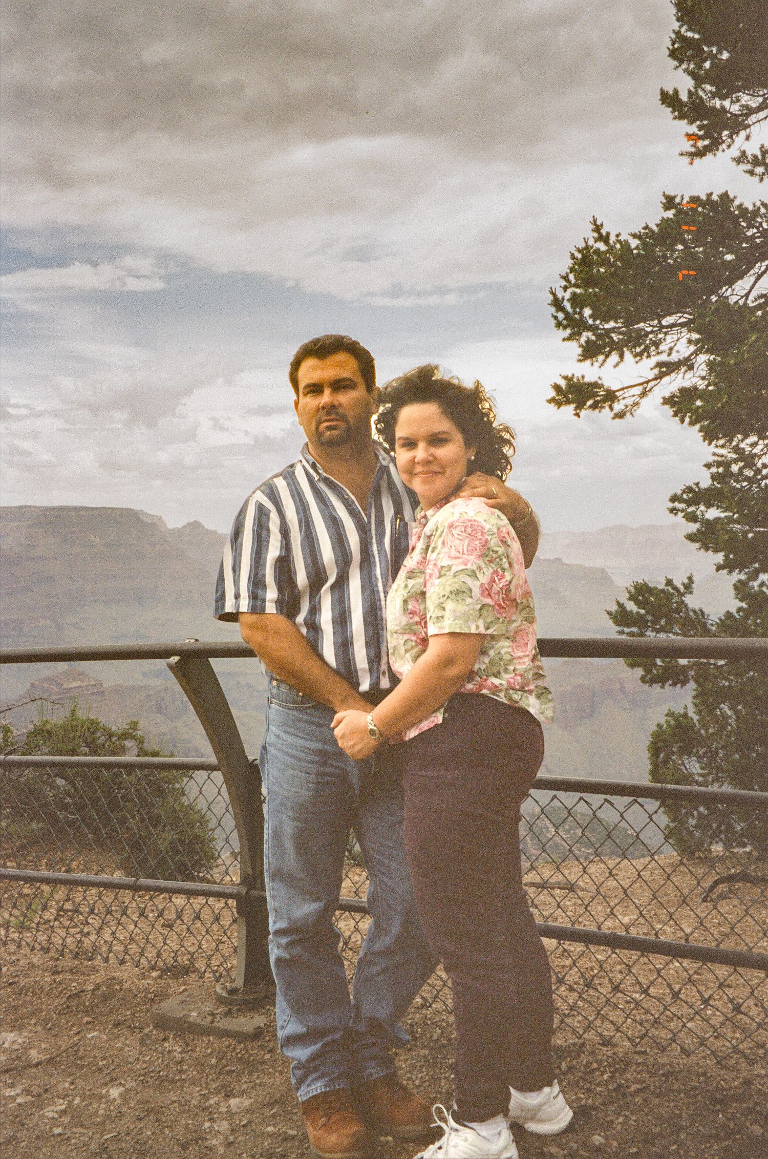 Couple standing at scenic canyon overlook with safety railing.