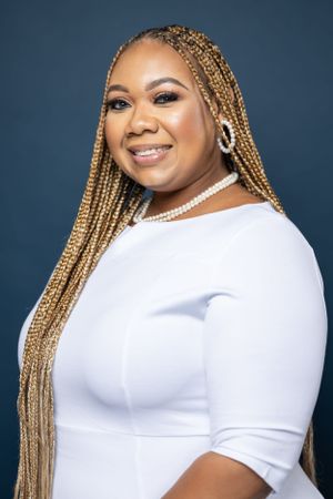 Professional photo with blonde braids, white fitted top and pearl necklace against dark backdrop.