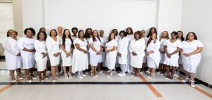 A large group of women wearing coordinated white outfits pose together for a formal photo.