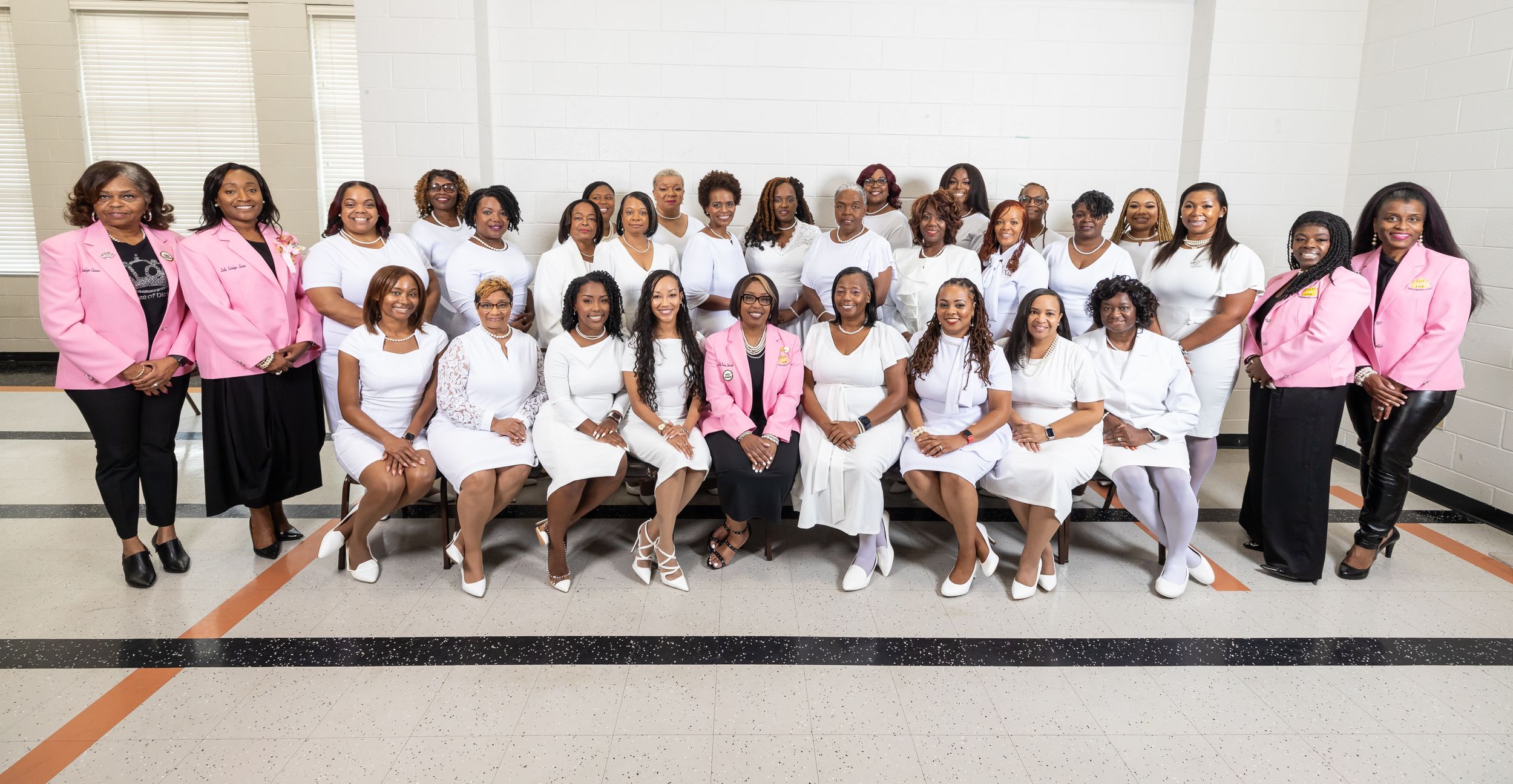 A group photo of women in white outfits with some members wearing pink jackets.