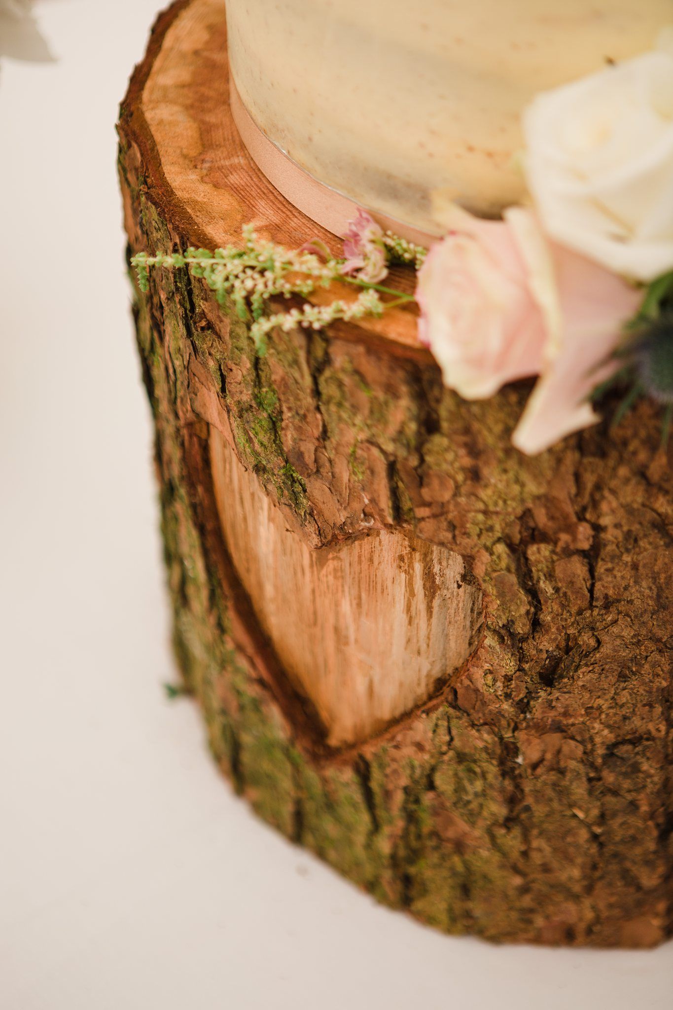 Rustic wedding cake displayed on a natural wood tree stump slice, adorned with pink roses and delicate white flowers.