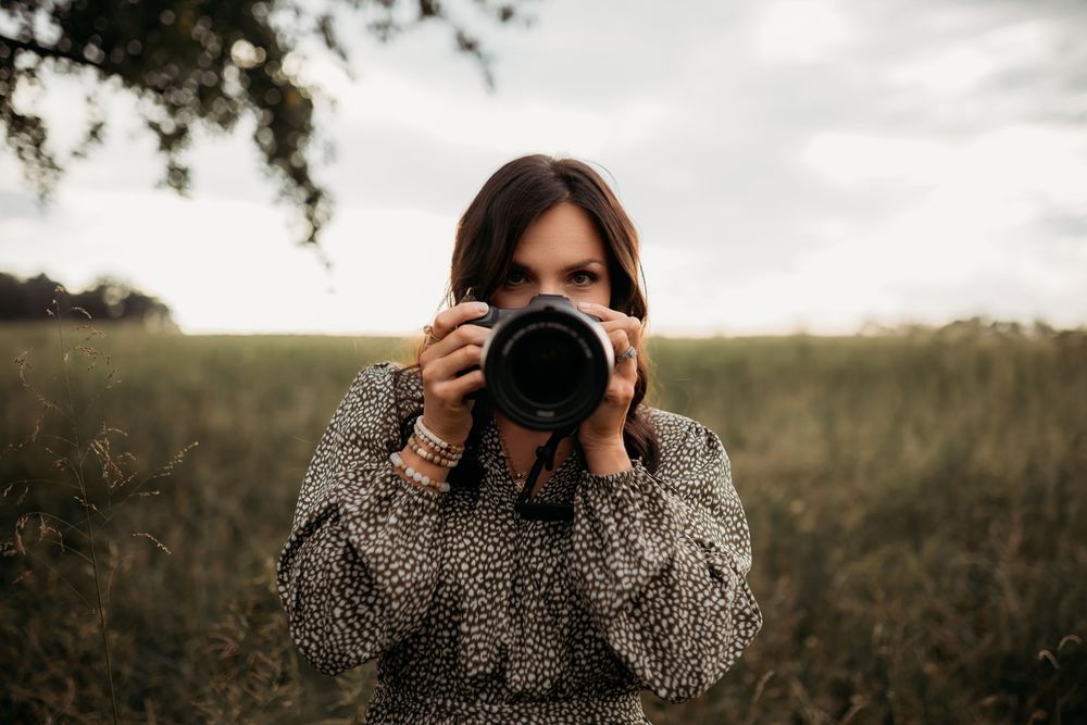 A person wearing a floral dress takes photos in a golden field during sunset.
