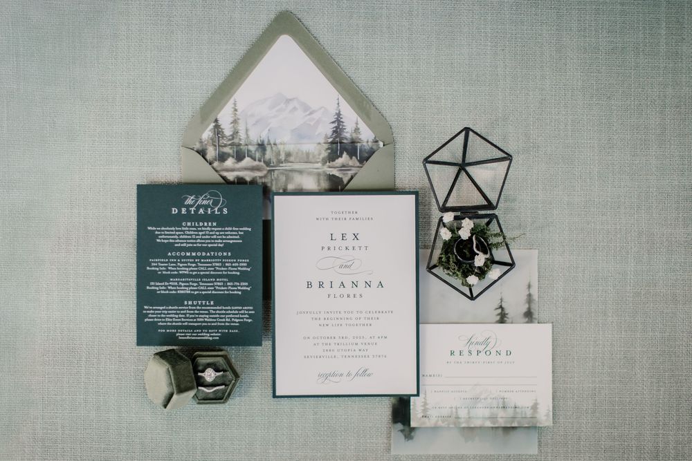 Elegant wedding invitation suite with mountain-illustrated envelope liner, green stationery, and geometric terrarium on gray background.