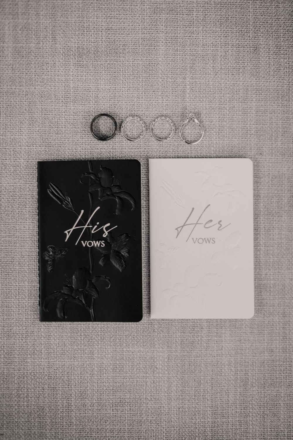 His and Her vows books with wedding rings on gray linen background.