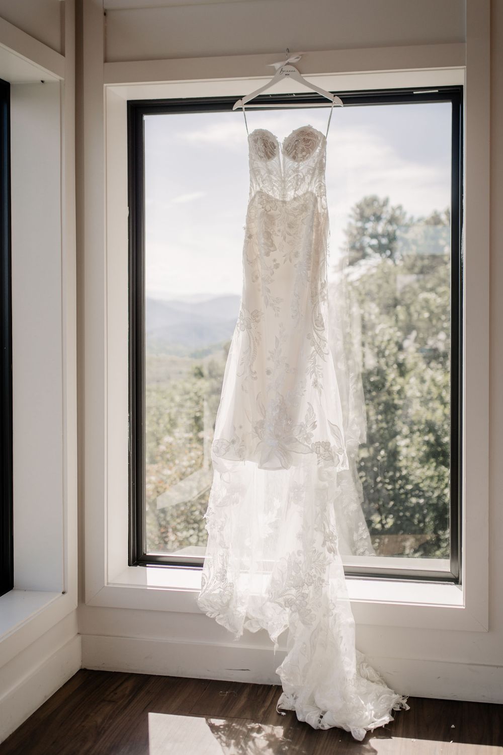 Elegant lace wedding dress hanging in a window with mountain views.