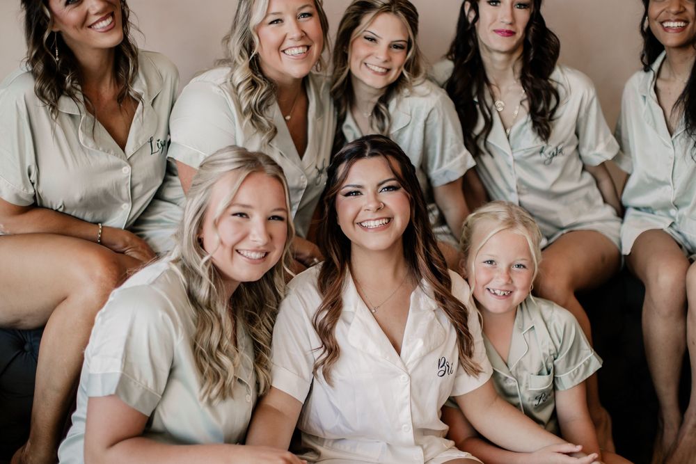 Close-up of bride and bridesmaids laughing in matching satin robes with young flower girl.