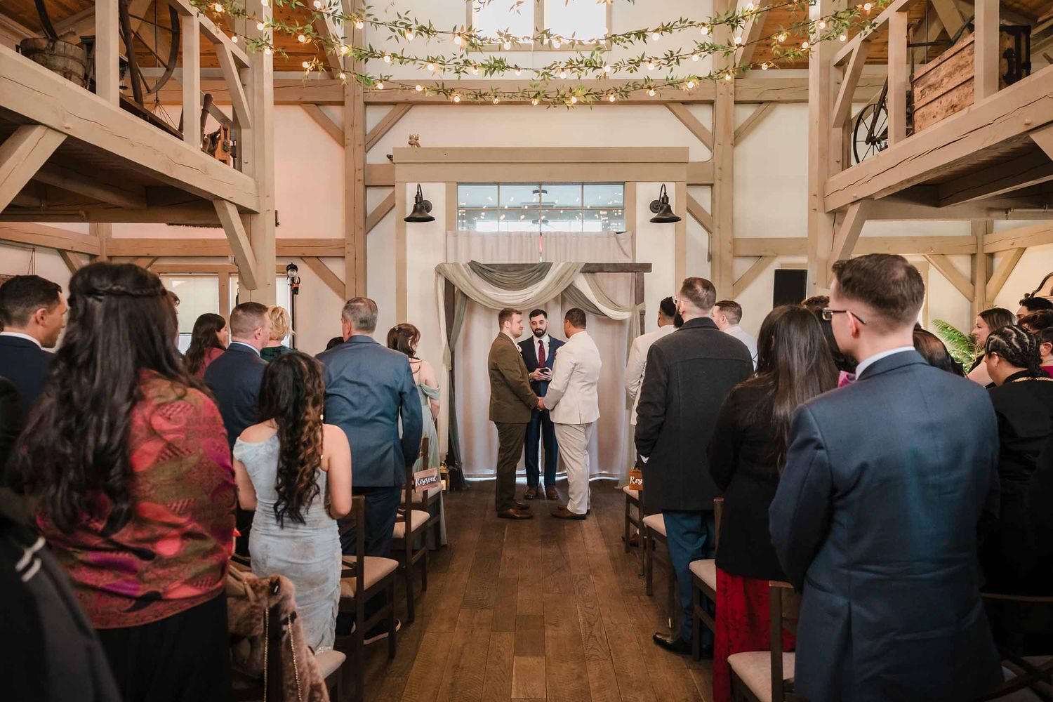 Guests standing during wedding ceremony at Briar Barn Inn indoor barn venue with aisle and greenery lights