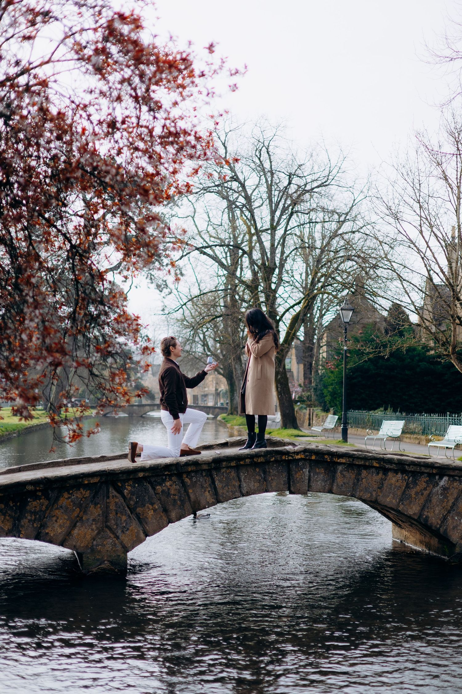 Couple sharing a romantic proposal moment at bourton on the water on a charming cotswolds bridge.