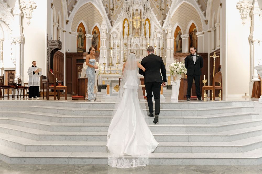 Bride and groom walk toward ornate white altar in an elegant Catholic church during wedding ceremony.
