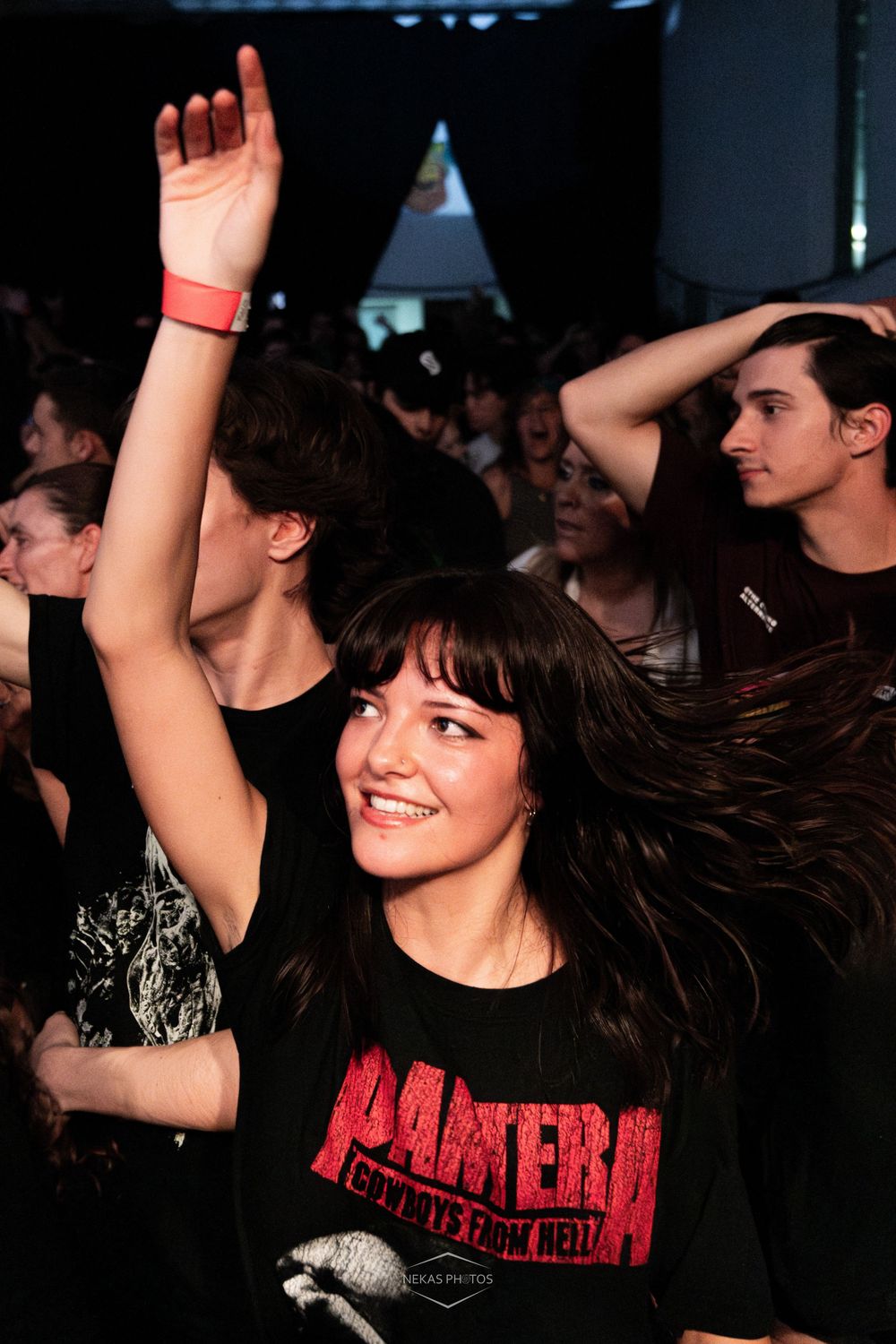Young woman in Pantera t-shirt smiling and dancing with hand raised at a live music concert.