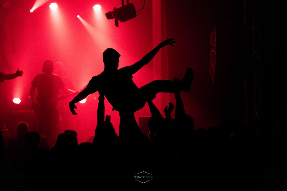 Crowd surfing silhouette at a rock concert with dramatic red stage lighting.