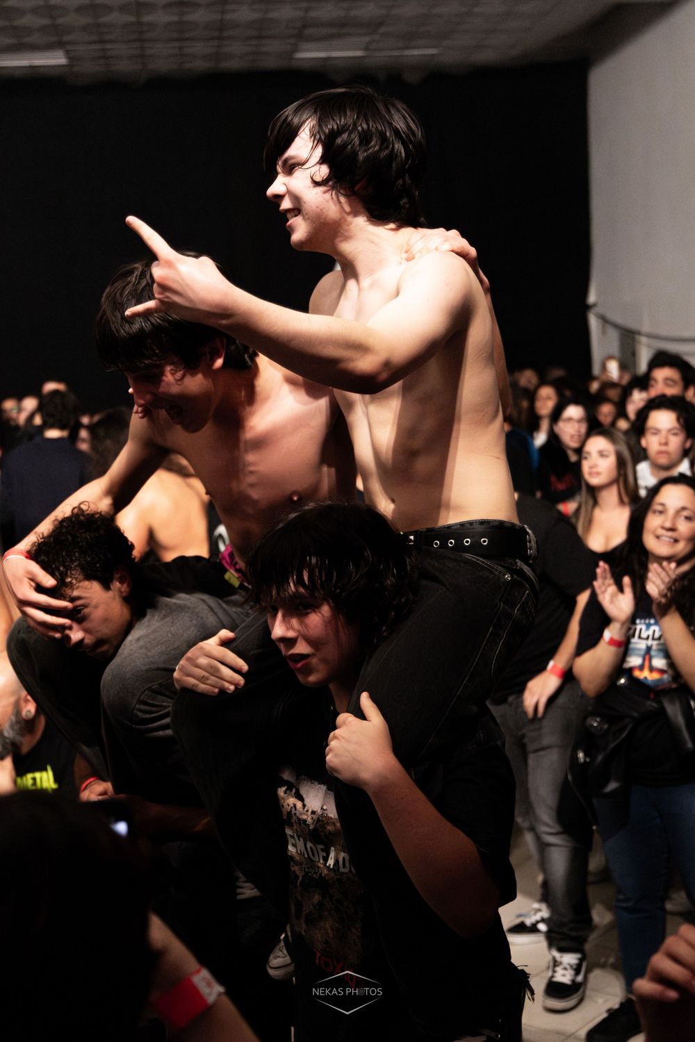 Shirtless young man crowd surfing on shoulders at a rock concert with energetic fans in background.