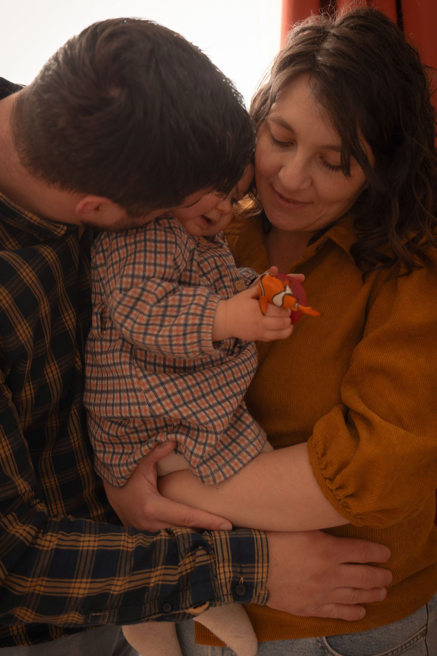 Portrait intimiste d'un couple enlaçant leur bébé, photographie de famille aux tons chauds et authentiques en Dordogne.