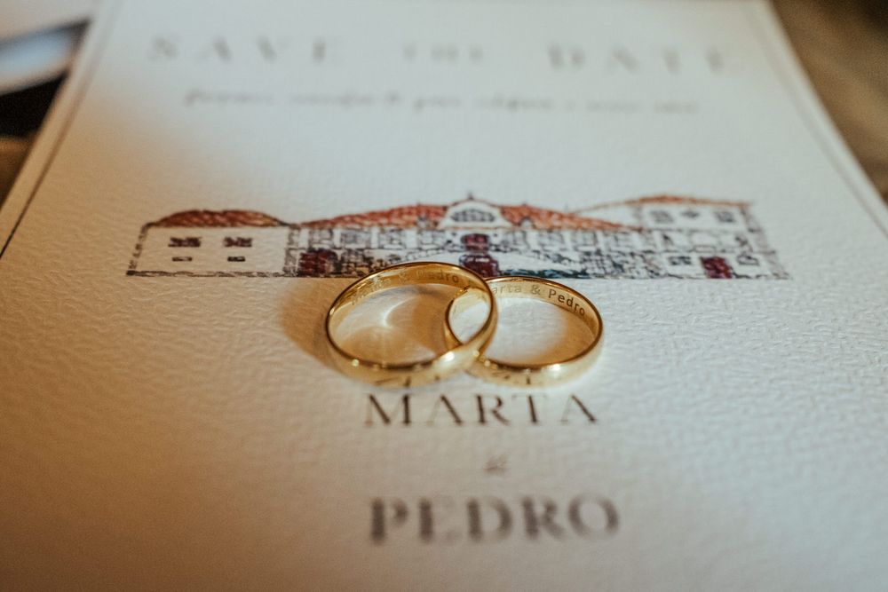 Two gold wedding rings on a save the date card for Maria and Pedro's wedding.